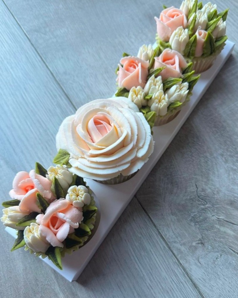 Row of blush and ivory buttercream rose cupcakes on a white gift tray