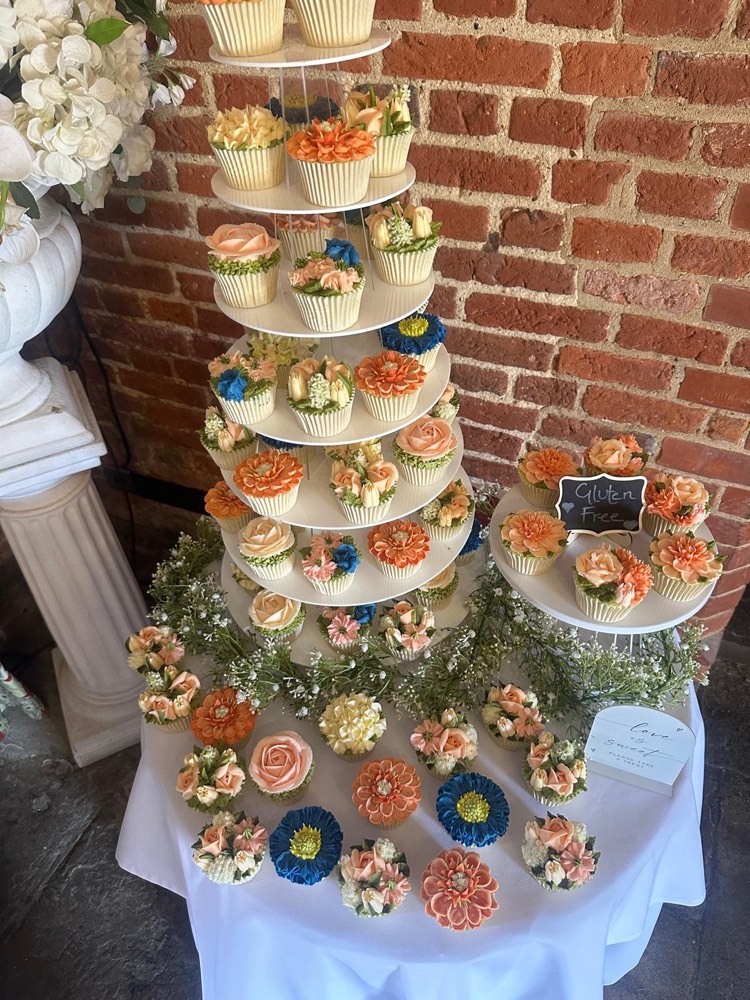 Wedding cupcake tower with orange, peach and blue buttercream flowers against a brick wall