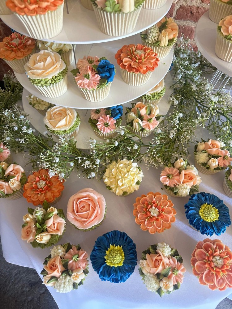 Close-up of orange dahlia, blue aster and peach rose buttercream cupcakes