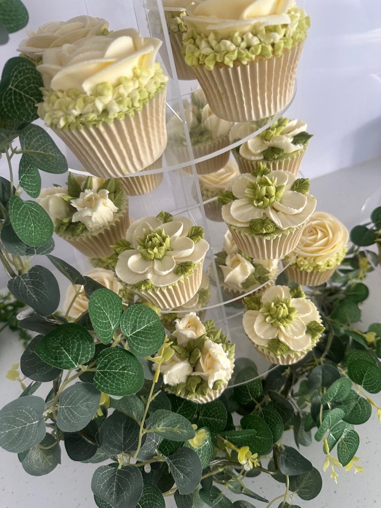 Ivory and sage buttercream floral cupcakes on a clear acrylic stand with eucalyptus garland