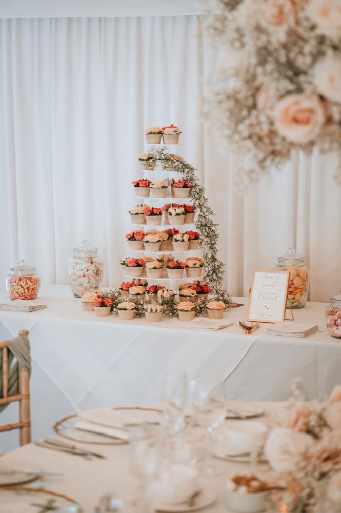 Wedding cupcake tower with coral and cream buttercream roses beside a sweet treat table