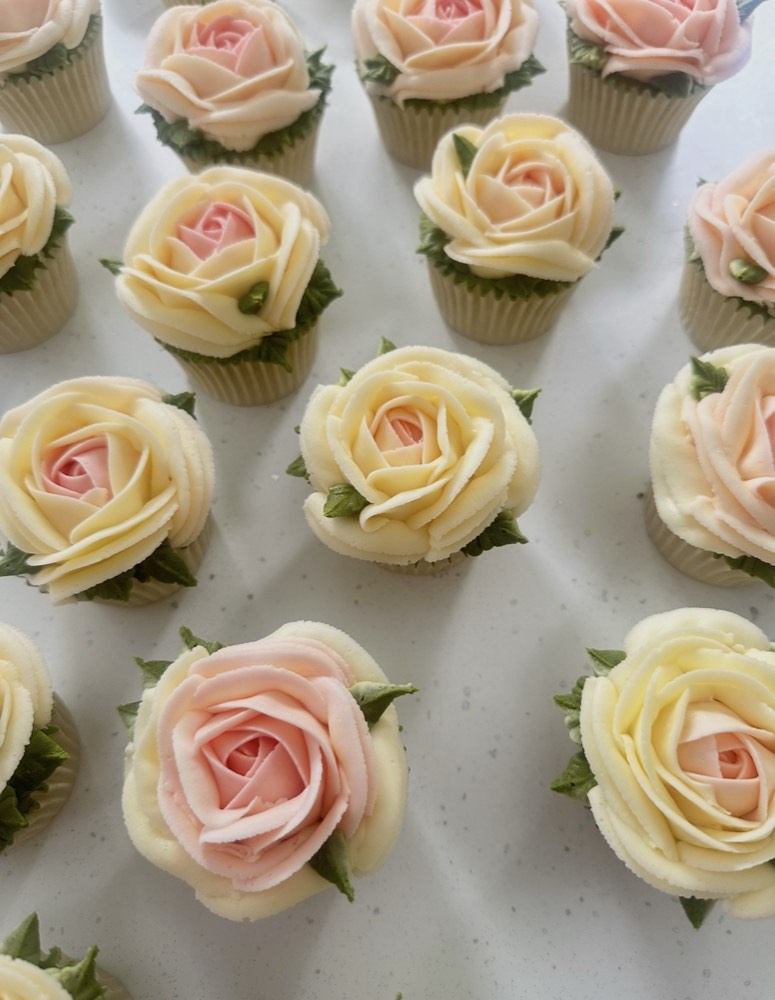 Close-up flat lay of ivory and blush buttercream rose cupcakes